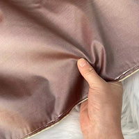 A hand pinches a piece of shiny, light brown taffeta silk from Longan Craft, highlighting its smooth texture and stiffness—ideal for luxurious evening gowns. High quality 100% mulberry silk fabric sold by the yard.