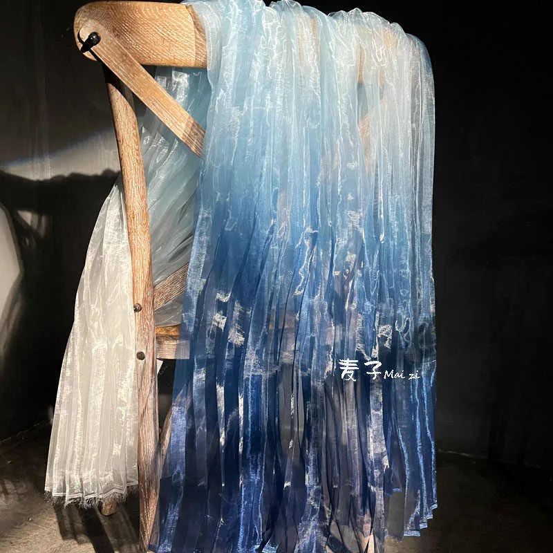 A wooden chair showcases Longan Craft’s Gradient Pleated Organza Fabric By The Yard, featuring a shiny finish in white to deep blue—ideal for wedding gowns—evoking elegance against a dark background.