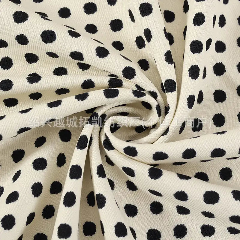 Close-up of the Longan Craft Polka Dot Print Corduroy Fabric By The Yard, featuring fine wale corduroy material in a cream color with irregular black dots, artfully gathered and twisted into a spiral to showcase its unique texture and playful retro dotted pattern—ideal for apparel and textile projects.