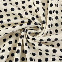 Close-up of the Longan Craft Polka Dot Print Corduroy Fabric By The Yard, featuring fine wale corduroy material in a cream color with irregular black dots, artfully gathered and twisted into a spiral to showcase its unique texture and playful retro dotted pattern—ideal for apparel and textile projects.
