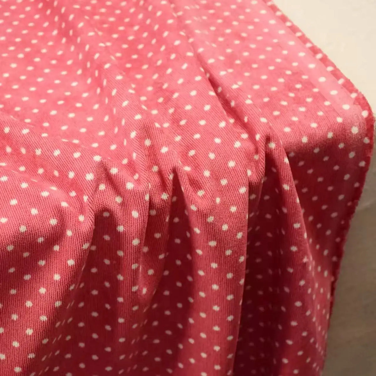 Pink Polka Dot Printed 21 Wales Corduroy Fabric By The Yard with a white polka dot pattern draped in folds.