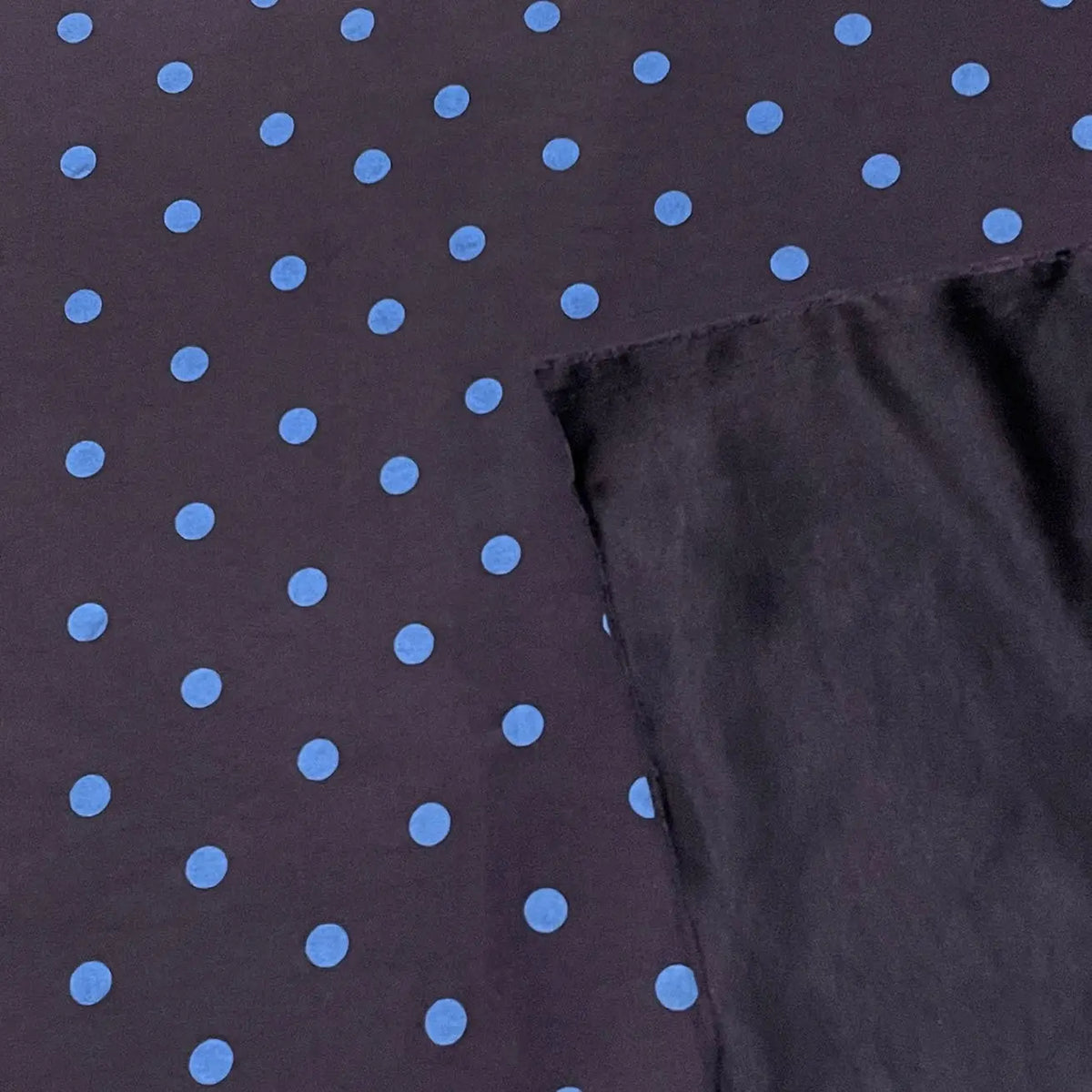 Polka Dot Printed Faux Suede Fabric By The Yard in dark faux suede with a pattern of light blue polka dots, shown with a folded corner revealing the solid dark underside.