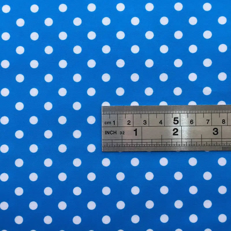 A metal ruler with inch and centimeter marks is placed on Longan Craft's Polka Dot Printed Peachskin Fabric By The Yard, a blue microfiber polyester fabric with white polka dots and a soft texture for DIY skirts.