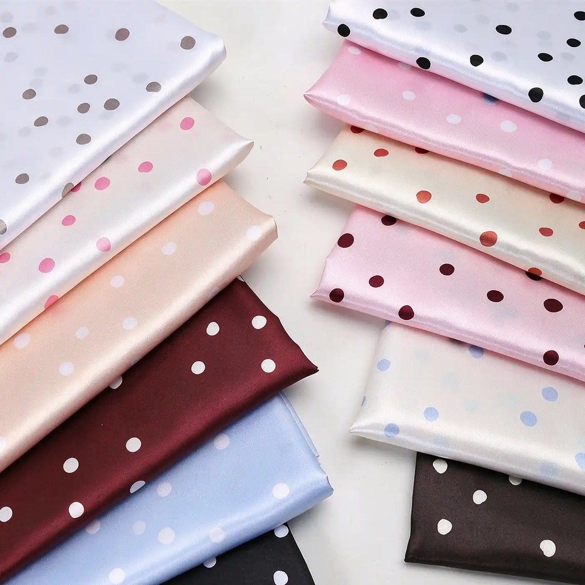Two stacks of folded Polka Dot Printed Satin Fabric By The Yard in various colors, perfect for dressmaking.