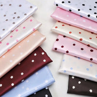 Two stacks of folded Polka Dot Printed Satin Fabric By The Yard in various colors, perfect for dressmaking.
