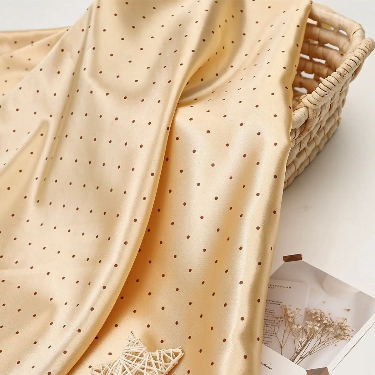 Cream-colored Polka Dot Printed Satin Fabric By The Yard draped over a woven basket.