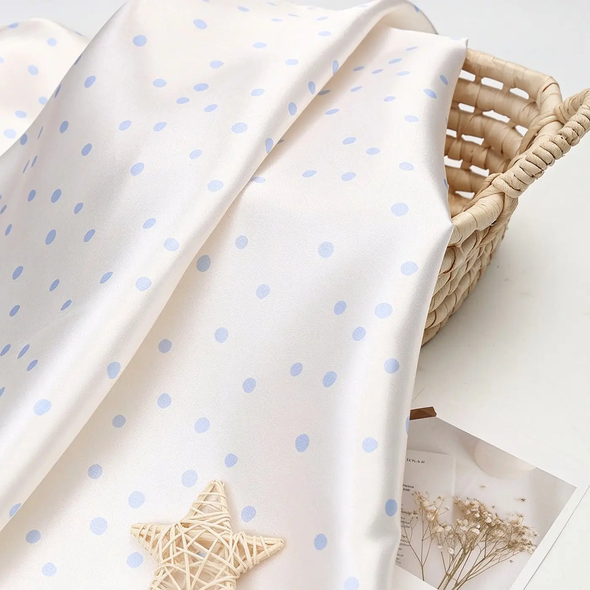 Off-white Polka Dot Printed Satin Fabric By The Yard draped over a woven basket.