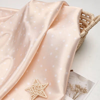 Pale peach polka dot Polka Dot Printed Satin Fabric By The Yard draped over a wicker basket.