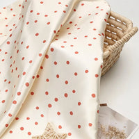 Off-white Polka Dot Printed Satin Fabric By The Yard with a red polka dot pattern draped over a woven basket.