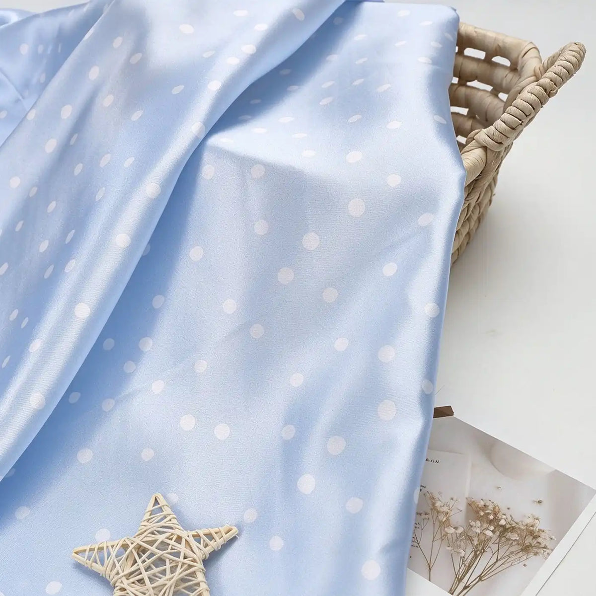Light blue Polka Dot Printed Satin Fabric By The Yard draped over a woven basket.