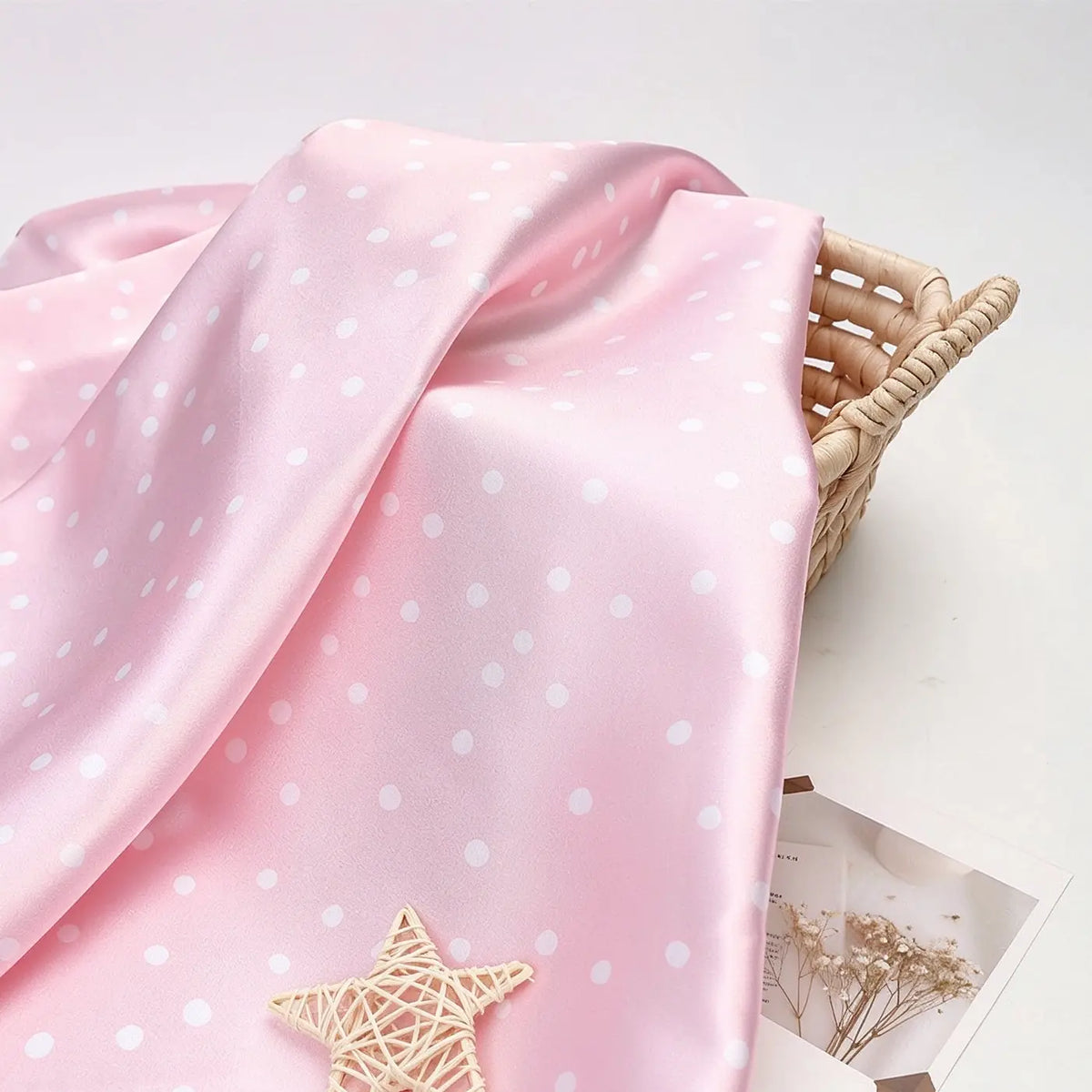 Light pink Polka Dot Printed Satin Fabric By The Yard with a white polka dot pattern draped over a woven basket.