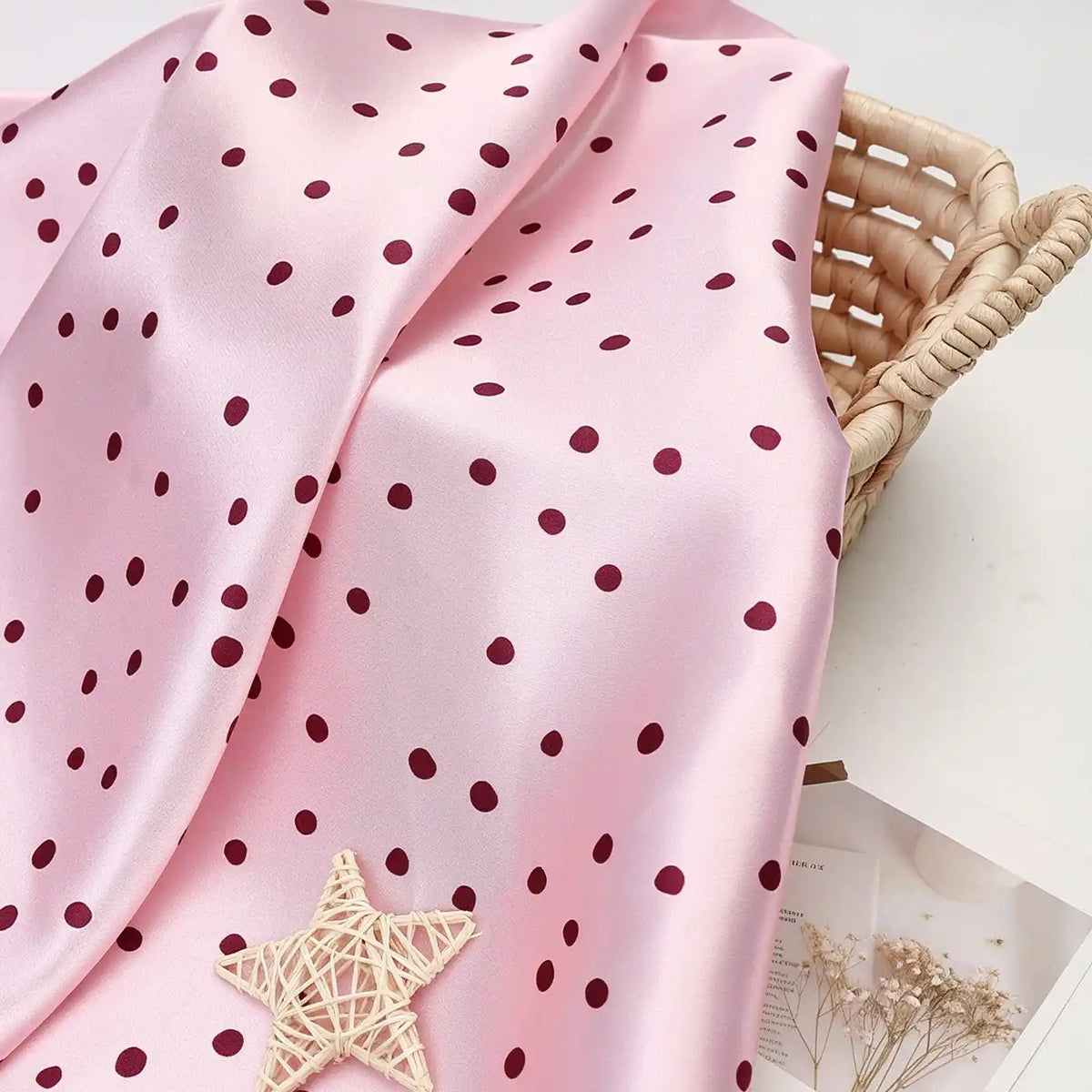 Light pink polka dot Polka Dot Printed Satin Fabric By The Yard draped over a wicker basket.