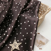 Polka Dot Printed Satin Fabric By The Yard in dark brown draped over a woven basket.