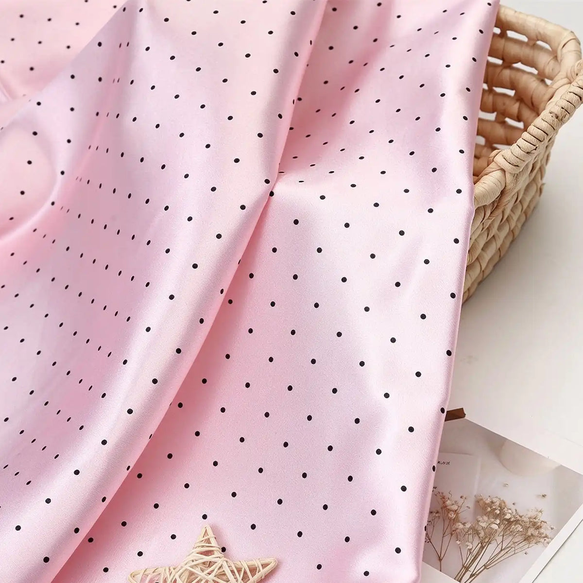 Polka Dot Printed Satin Fabric By The Yard in light pink with small black polka dots draped over a woven basket.