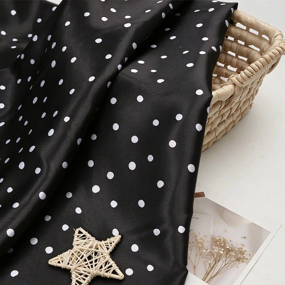 Black polka dot Polka Dot Printed Satin Fabric By The Yard draped over a wicker basket.