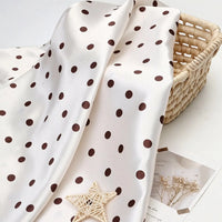 Polka Dot Printed Satin Fabric By The Yard in white draped over a woven basket.