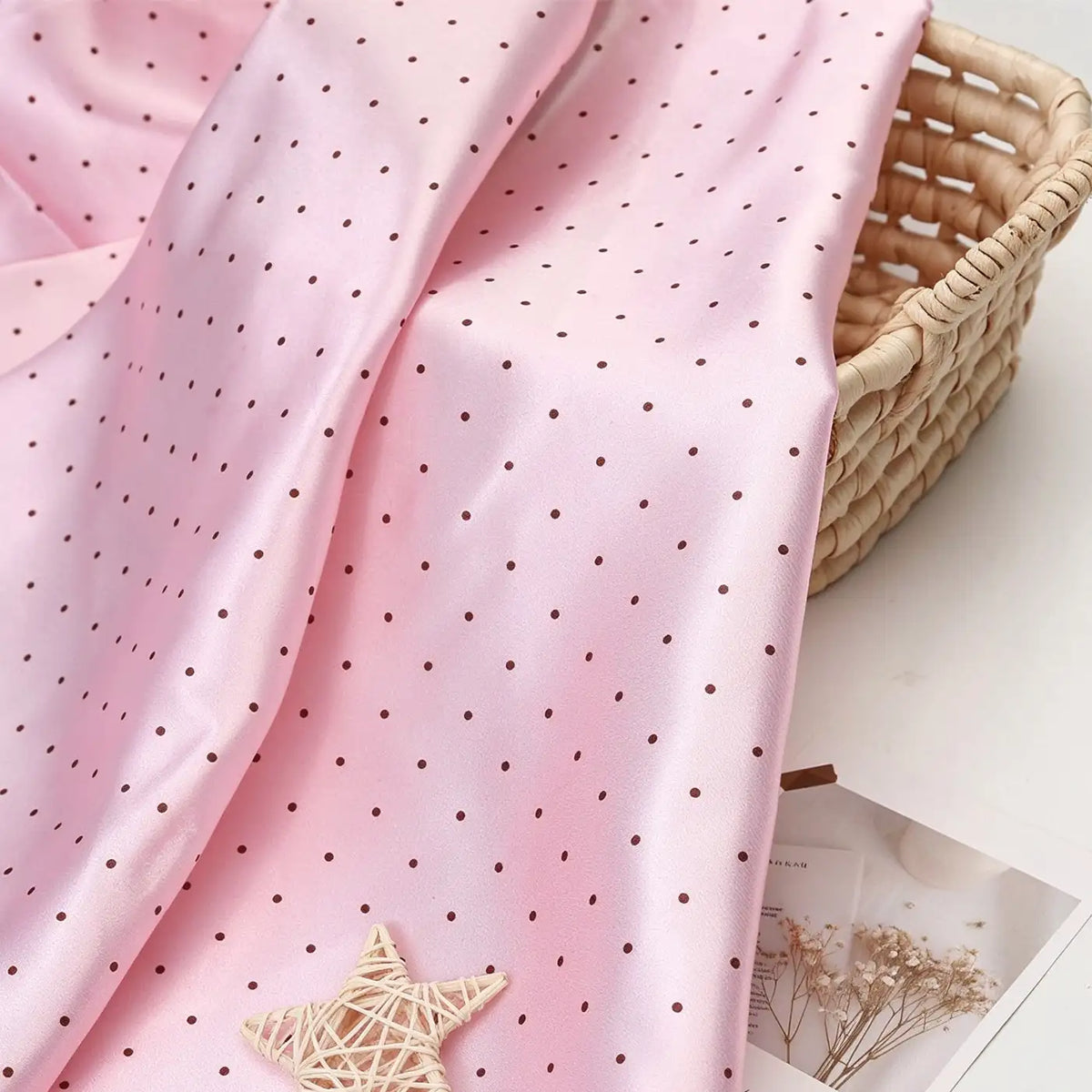 Light pink polka dot Polka Dot Printed Satin Fabric By The Yard draped over a woven basket.