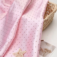 Light pink polka dot Polka Dot Printed Satin Fabric By The Yard draped over a woven basket.
