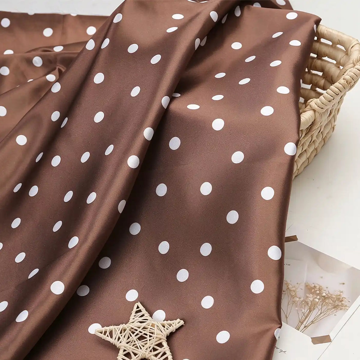 Brown polka dot Polka Dot Printed Satin Fabric By The Yard draped over a woven basket.