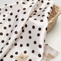 Off-white Polka Dot Printed Satin Fabric By The Yard draped over a woven basket.