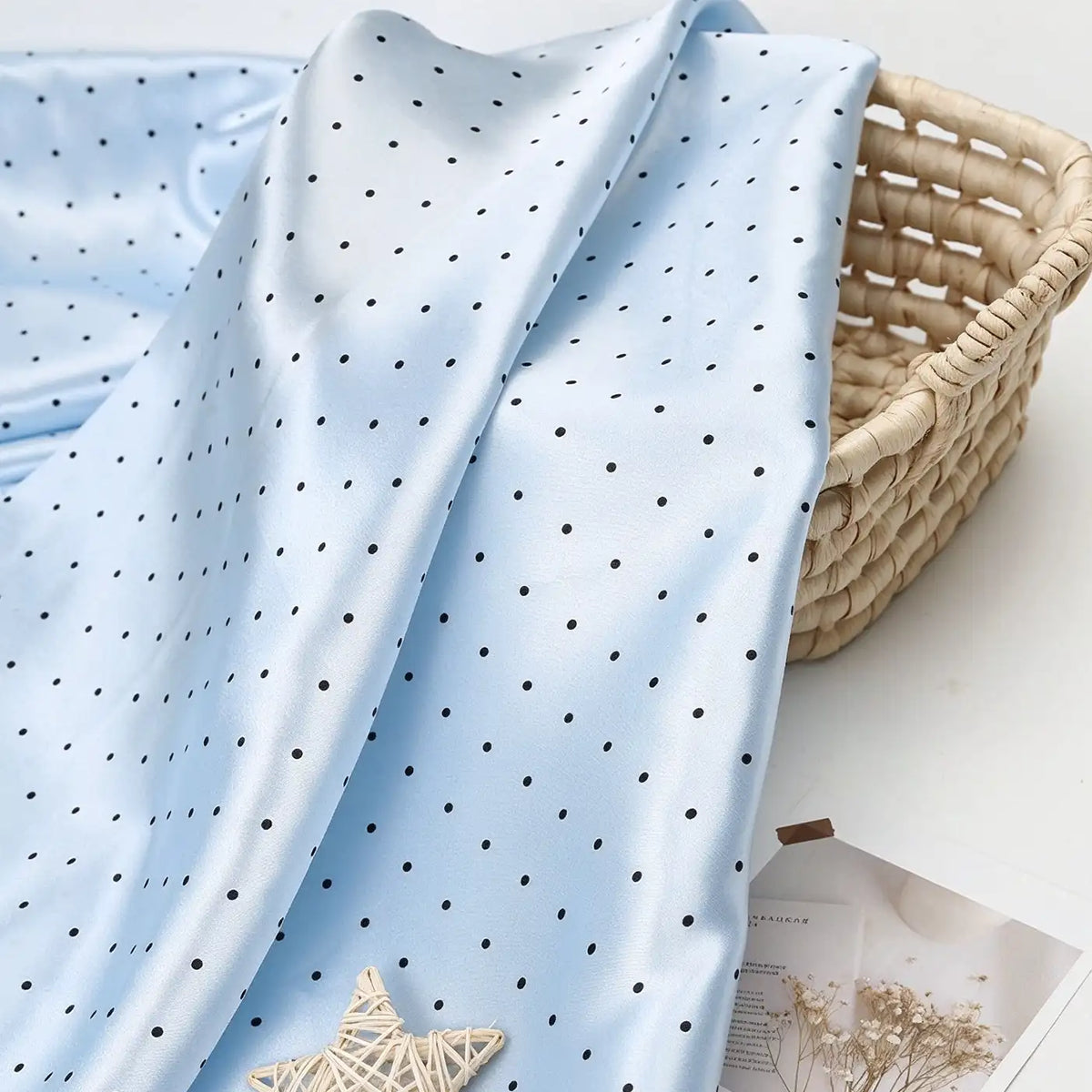 Light blue polka dot Polka Dot Printed Satin Fabric By The Yard draped over a woven basket.