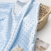 Light blue polka dot Polka Dot Printed Satin Fabric By The Yard draped over a woven basket.