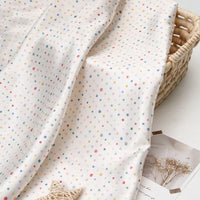 Polka Dot Printed Satin Fabric By The Yard in white draped over a woven basket.