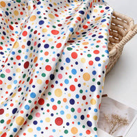 Polka Dot Printed Satin Fabric By The Yard in white draped over a woven basket.