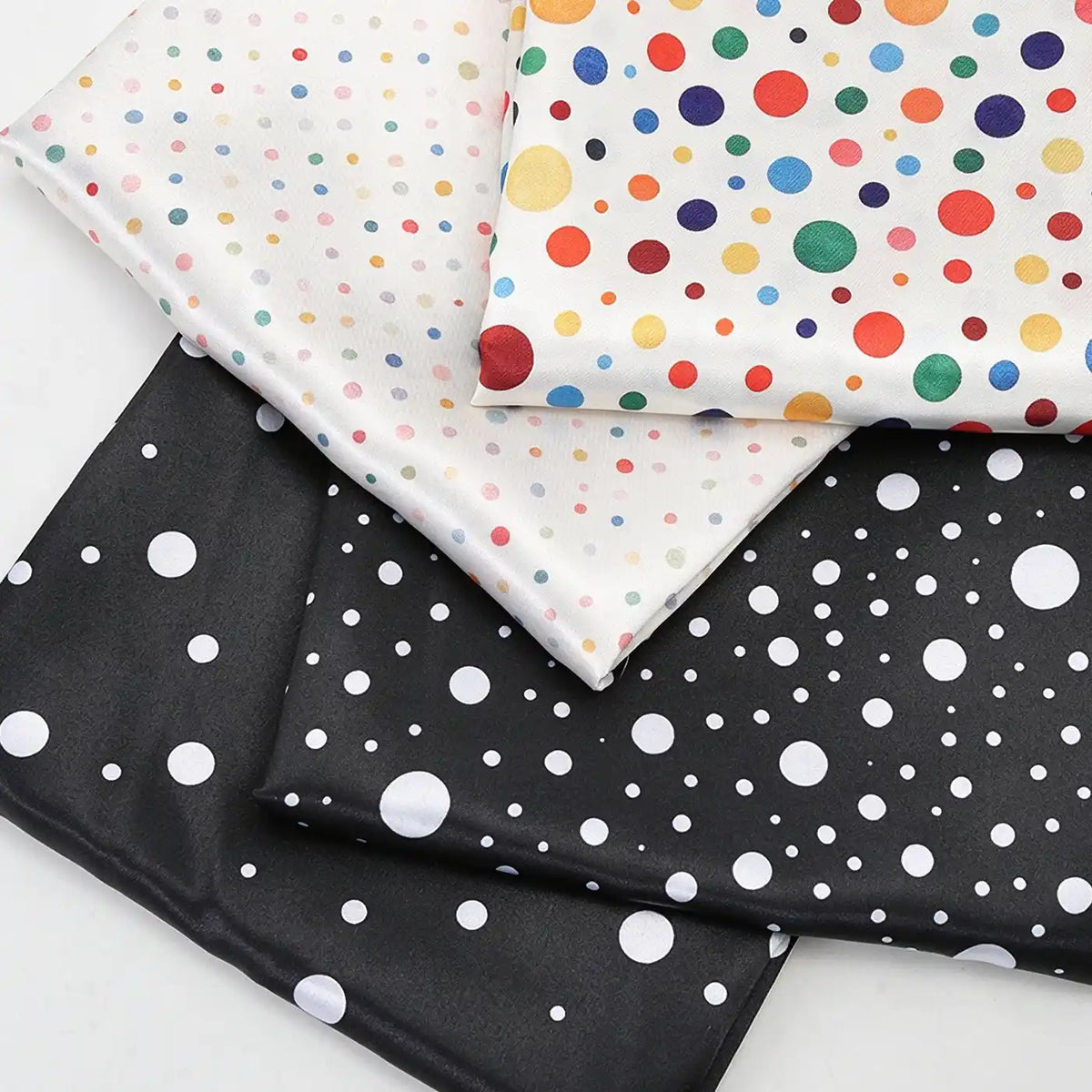 Four folded pieces of Polka Dot Printed Satin Fabric By The Yard featuring various sizes and colors of polka dot patterns.