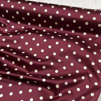 Longan Craft’s Polka Dot Stretch Silk Fabric By The Yard (19 Momme) features a maroon base with white polka dots and a shiny finish, draped in gentle folds—ideal vintage silk fabric for evening gowns and clothing.
