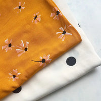 Two pieces of Longan Craft viscose fabric are shown: a mustard yellow floral print and a white fabric with bold black polka dots, both folded neatly. These 100% viscose prints are ideal for long skirts and sold by the yard.