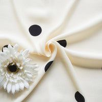 A softly gathered Polka Dot and Floral Printed Viscose Fabric By The Yard from Longan Craft, featuring elegant cream with bold black dots, is accented by a white artificial flower—perfect for fashionable long skirts.