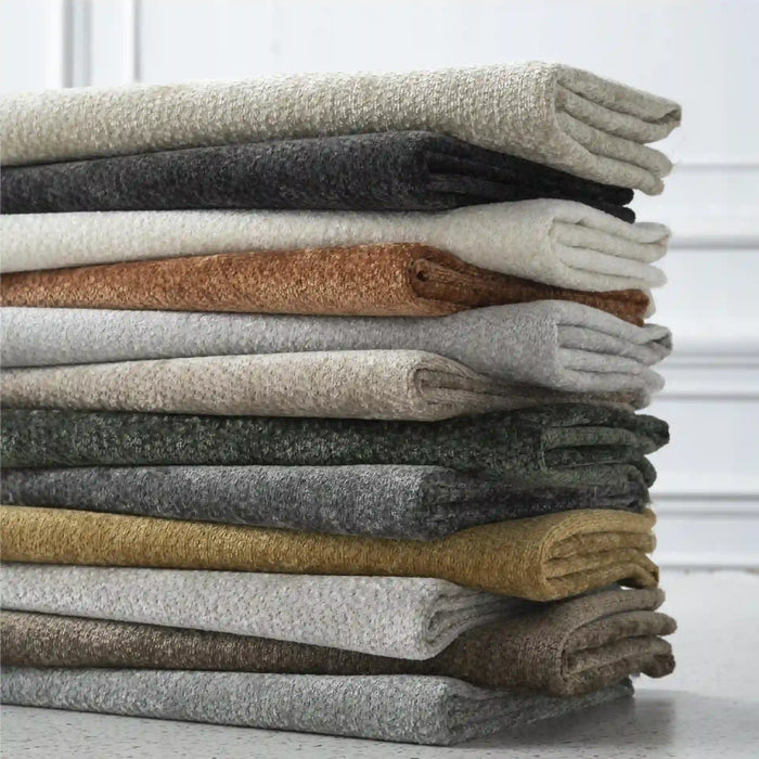 A neatly stacked pile of Longan Craft's solid color Poly Chenille Upholstery Fabric, featuring soft, stain-resistant chenille material, rests on a white surface in front of a white wall.
