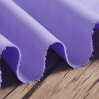 Close-up of Longan Craft Polyester Gabardine Fabric By The Yard, a soft light purple plain twill textile with a smooth, wrinkle-resistant texture and frayed edges, elegantly draped on wood—ideal for stylish jackets.