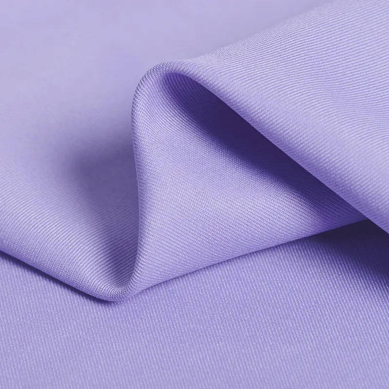 A close-up of Longan Craft’s Polyester Gabardine Fabric By The Yard shows smooth, wrinkle-resistant light purple twill with soft folds and fine diagonal lines—ideal premium material for stylish jackets.