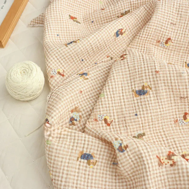 The Puppy Print Gingham Double Gauze Fabric by Longan Craft features brown plaid pure cotton with playful puppy prints, displayed on a quilted surface with cream yarn—perfect for breathable sleepwear, baby clothes, or crafts.