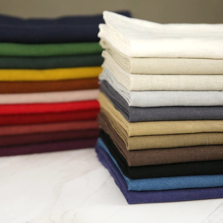 A tidy stack of Pure Color 100 Linen Fabric By The Yard from Longan Craft, featuring a range of colors including white, cream, brown, red, yellow, green, and blue is neatly arranged on a light surface. Each piece displays the beautiful medium weight 100% linen material—perfect for casual wear and renowned for its breathable comfort.