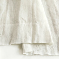 A close-up of Pure Color 100 Linen Fabric by Longan Craft, a medium weight, 100% linen material in a natural off-white shade, highlighting its soft texture and gentle folds on a light surface—perfect for comfy casual wear.