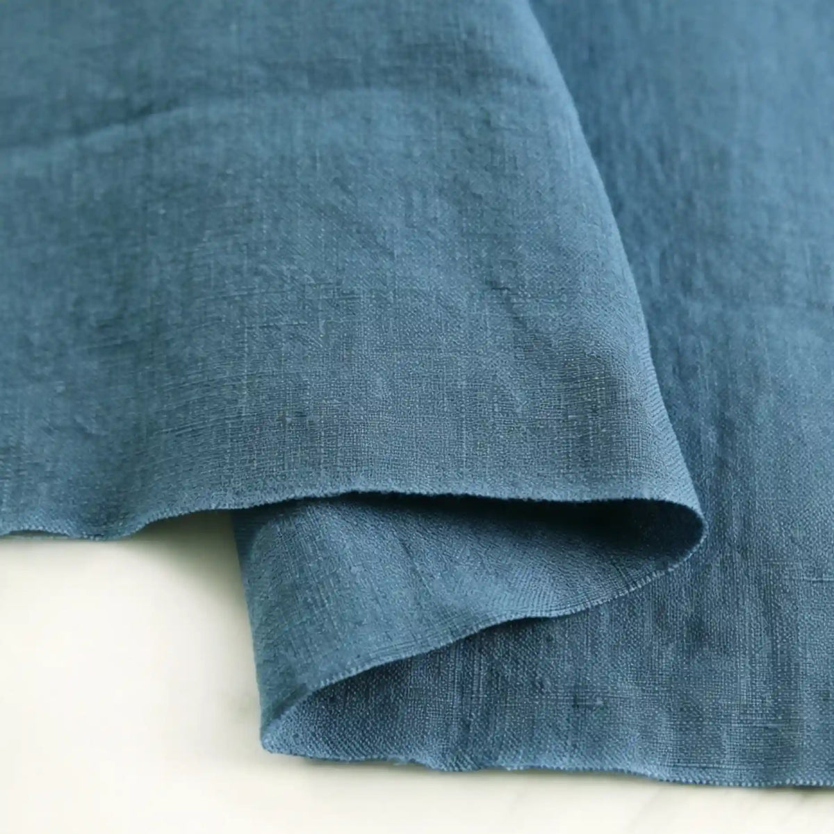 A close-up of Longan Craft’s Pure Color 100 Linen Fabric By The Yard, a medium weight linen material with a soft texture, shown folded on a light surface.