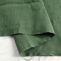 A piece of Longan Craft Pure Color 100 Linen Fabric by the yard, a medium weight, comfy linen material for casual wear, is displayed on a light-colored marble surface, highlighting its natural texture and slightly frayed edges.