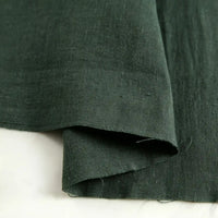 A close-up of Longan Craft’s Pure Color 100 Linen Fabric By The Yard in dark green, highlighting its natural texture and medium-weight weave with two overlapping layers displayed on a white surface—perfect for comfy, casual wear.