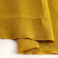 A close-up of Pure Color 100 Linen Fabric By The Yard from Longan Craft in mustard yellow, showcasing its visible weave texture; the medium weight linen clothing material is softly folded and displayed on a light surface.