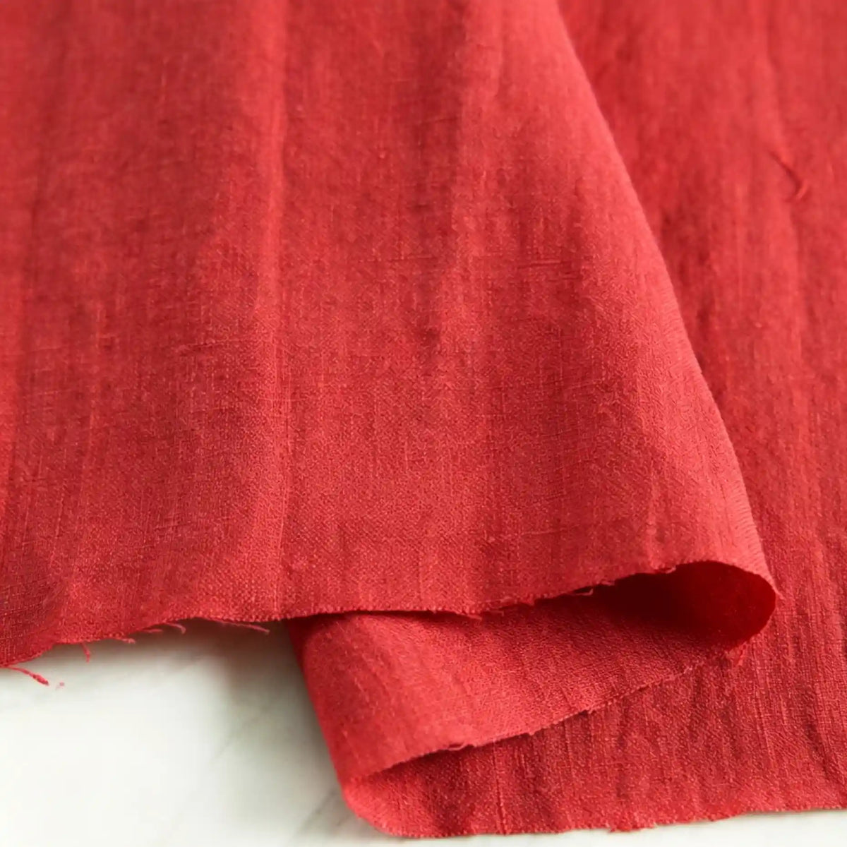 A close-up of Longan Craft’s Pure Color 100 Linen Fabric by the yard in a solid red shade, draped on a white surface to showcase its medium weight texture and natural weave—ideal for comfortable casual wear.