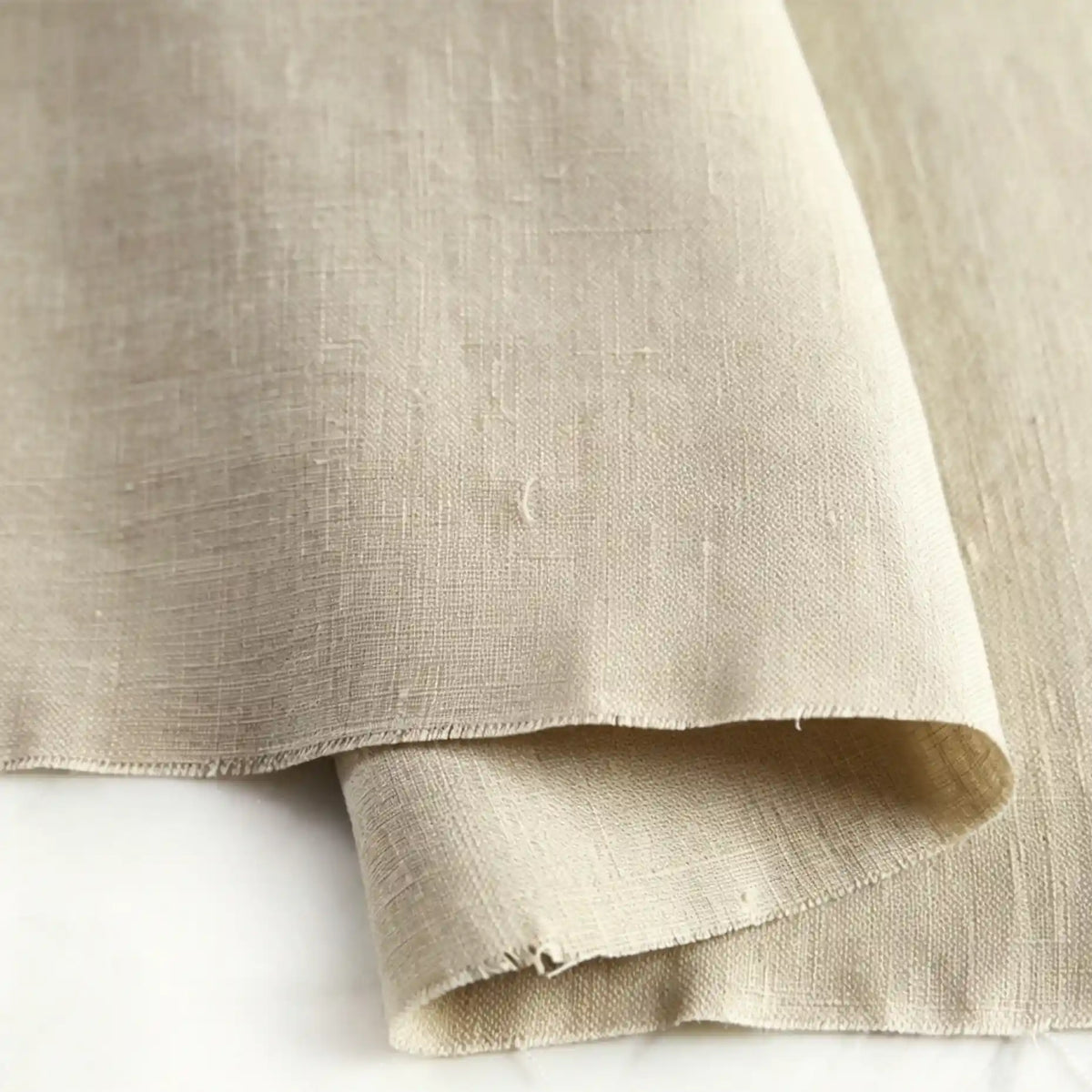 A close-up of Longan Craft’s Pure Color 100 Linen Fabric By The Yard showcases its natural texture, medium-weight weave, and subtle wrinkles. This comfy, 100% linen material is gently folded and displayed on a light-colored surface—perfect for casual clothing projects.