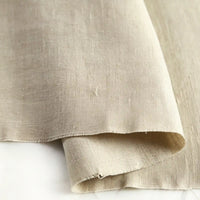 A close-up of Longan Craft’s Pure Color 100 Linen Fabric By The Yard showcases its natural texture, medium-weight weave, and subtle wrinkles. This comfy, 100% linen material is gently folded and displayed on a light-colored surface—perfect for casual clothing projects.