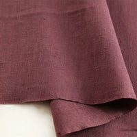 A close-up of Longan Craft’s Pure Color 100 Linen Fabric by the yard in mauve, highlighting its comfy medium-weight texture and natural weave, with one edge gently folded over itself on a light-colored surface—perfect for casual wear and clothing projects.