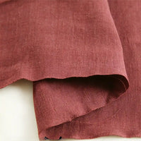 A close-up of Pure Color 100 Linen Fabric By The Yard from Longan Craft, in a reddish-brown shade, showcases its textured natural weave and slightly uneven edges as it rests on a light-colored surface. This medium weight, comfy linen material is ideal for casual wear and other sewing projects.