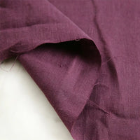 A close-up of a piece of Pure Color 100 Linen Fabric by the Yard from Longan Craft, shown in deep purple, features its medium weight and comfy texture with visible wrinkles and folds on a white surface.