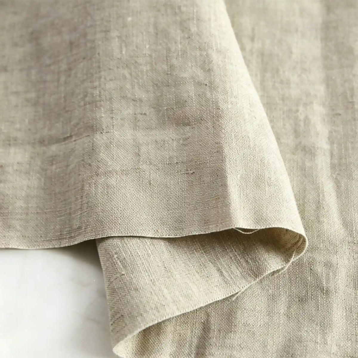 A close-up of Longan Craft’s Pure Color 100 Linen Fabric By The Yard in natural beige, folded to showcase its medium weight, visible texture, and weave details—ideal for comfy casual wear.