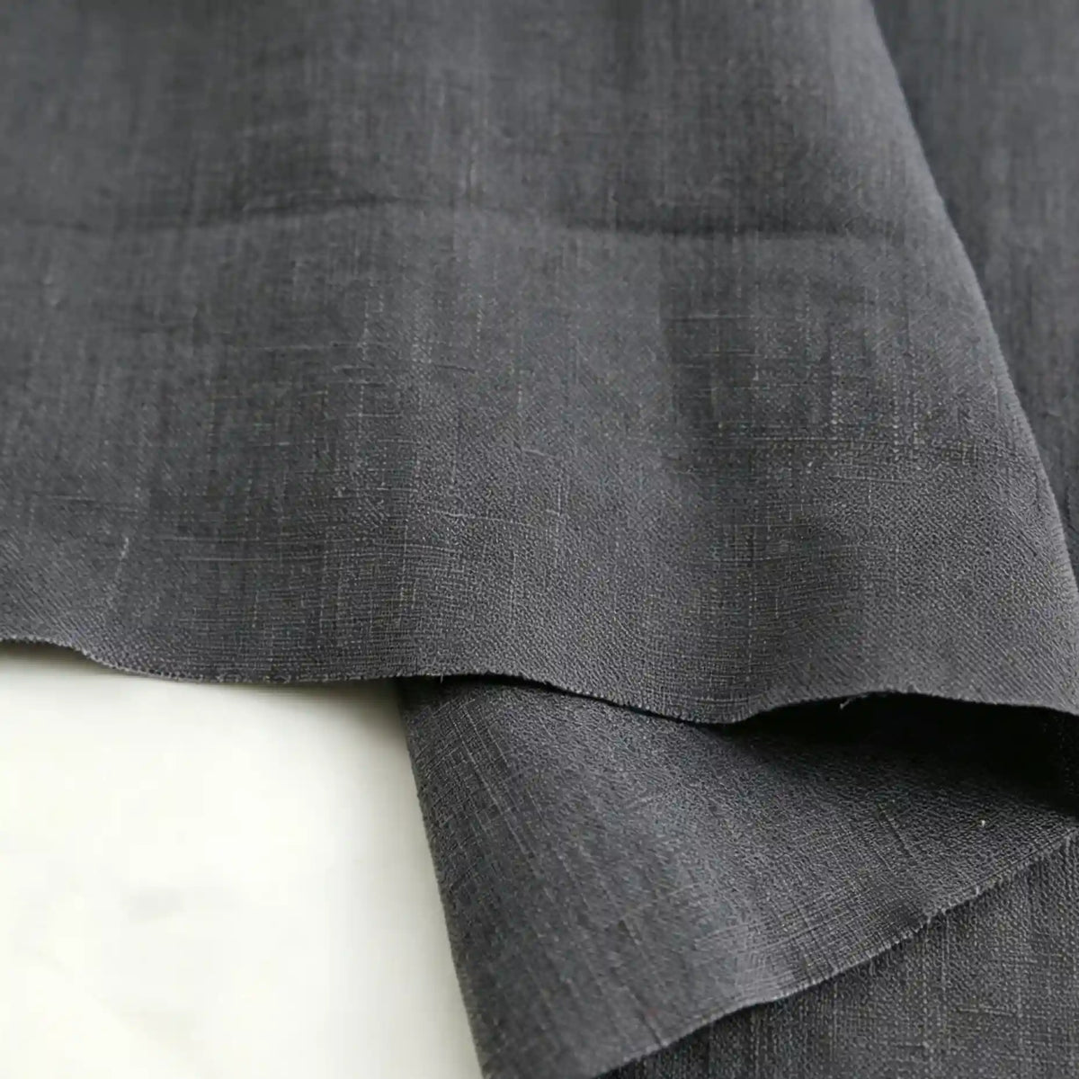 Two pieces of Longan Craft’s “Pure Color 100 Linen Fabric By The Yard,” crafted from 100% natural linen, overlap on a light surface, highlighting their soft texture and subtle weave pattern.